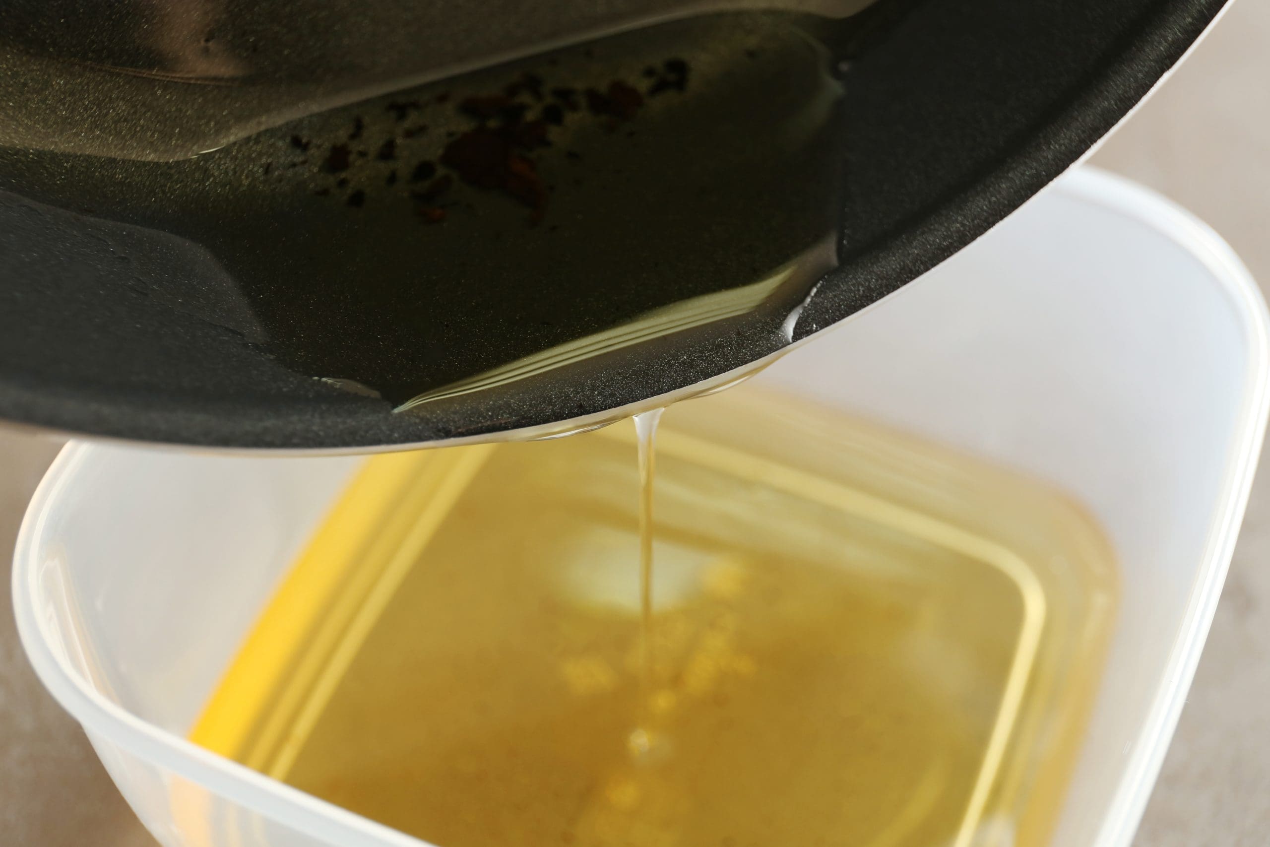Used cooking oil being poured from pan into container for recycling